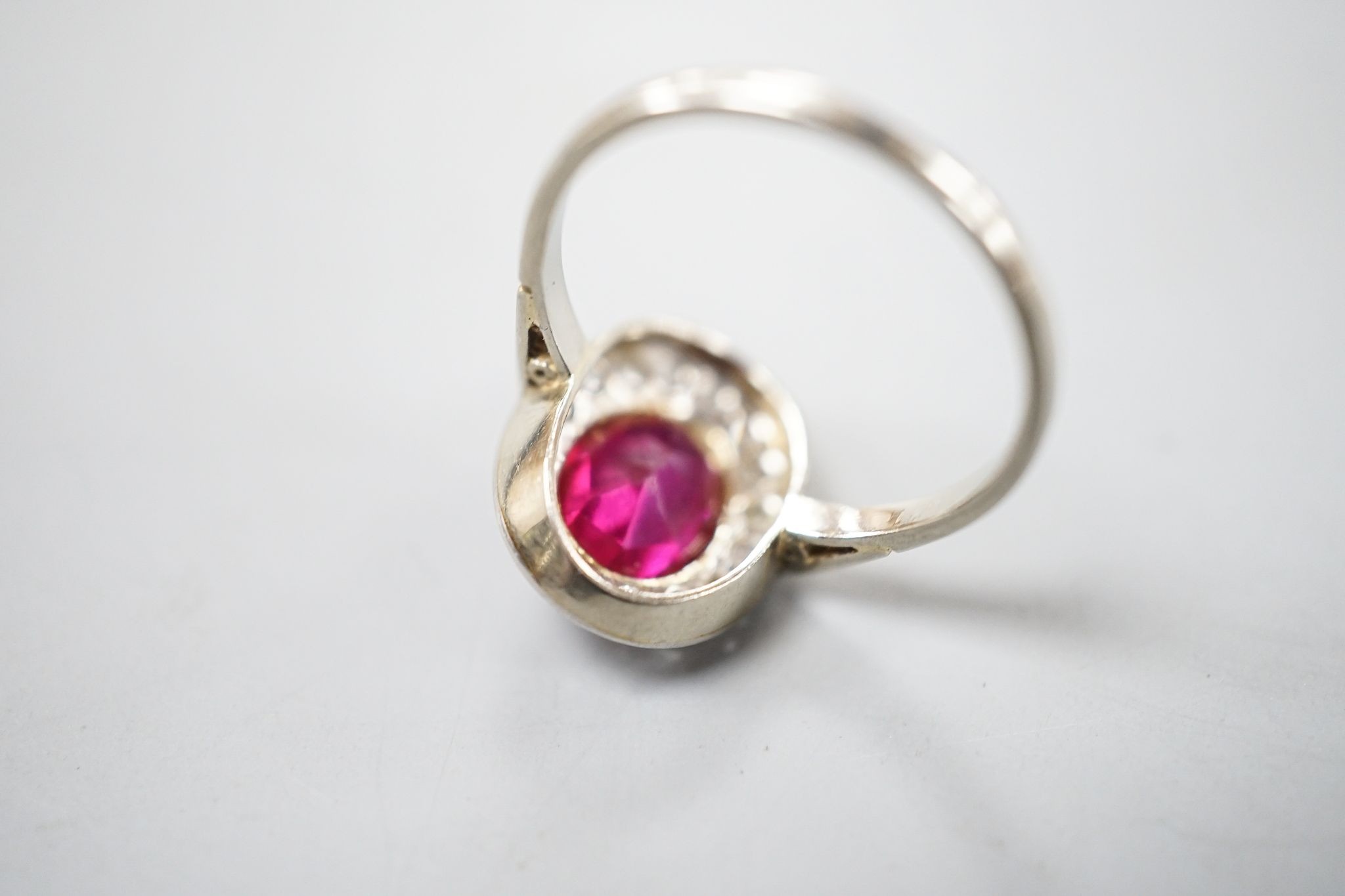 A white metal, synthetic ruby and diamond set oval cluster ring, size N, gross weight 3.4 rams.